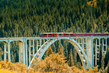 red train crosses a long viaduct across a deep ravine in the Swiss Alps