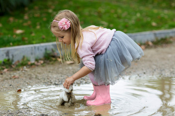 Beautiful little girl in a tutu skirt batting a teddy bear in a puddle on the street