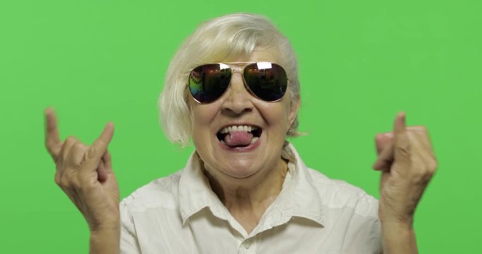 An elderly woman show sign of the horns with her hands and showing tongue
