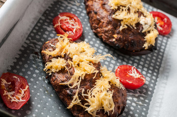 Baked eggplant with cheese and slices of tomato in square metal chafing dish on brown rustic wooden table
