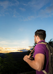 Naklejka premium Young Man enjoys the scene of nature during sunset at the mountains. He is hiking with a backpack. 