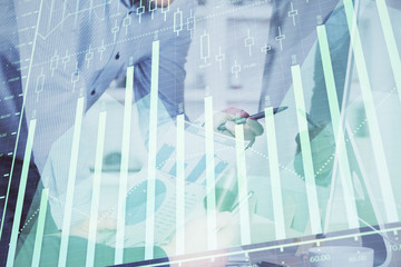 Double exposure of chart with businessman typing on computer in office on background. Concept of hard work.