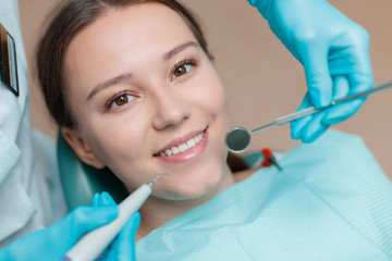 Patient in dental chair. Dentist's hands with blue gloves work with a dental tools. Beautiful young woman having dental treatment at dentist's office.