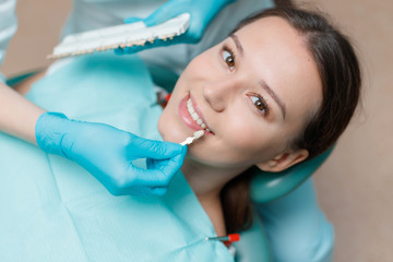 White teeth and beautiful smile of young woman. Matching the shades of the implants using shade guide. Preparation for teeth whitening in dental office. Patient in dental chair.