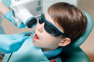 Dentist takes jaw x-ray. Patient in dental chair. Dentist's hands with blue gloves work with a...