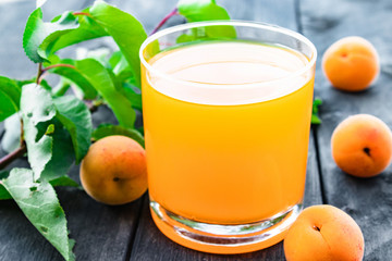 Fresh apricot juice with apricots and a branch with green leaves on the background of old boards.