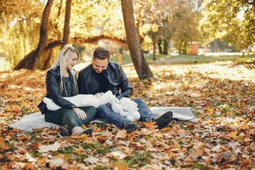 Family in a autumn park. Woman in a black jacket. Cute newborn little girl with parents