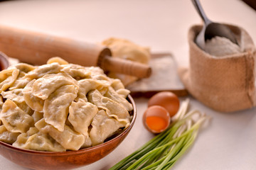 ready-made dumplings Ukrainian national dish in a clay dish on a board with ingredients eggs, flour and greens