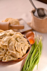 ready-made dumplings Ukrainian national dish in a clay dish on a board with ingredients eggs, flour and greens
