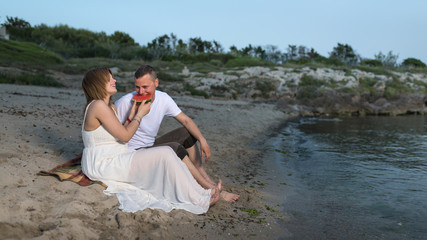 Pregnant couple on the beach, sitting on the sand. Picnic with watermelon.