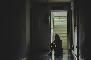 Silhouette of girl sitting alone in the dark,Sad and Serious women sitting hug his knee alone of old condo, Domestic violence, family problems, The concept of depression and suicide with copy space