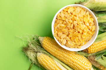 Corn flakes in white bowl near Corn Cobs