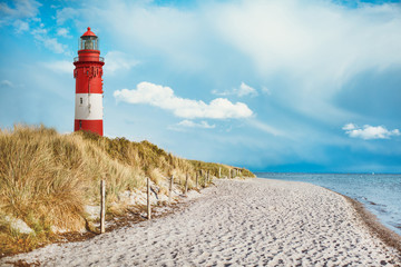 Leuchtturm am Strand einer Insel, an der Küste hinter und auf Düne mit Strandsand und Wasser am...