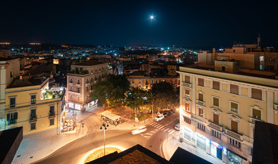 Piazzale Umberto I, Cagliari, Italy. Night view from the top of the city. Dark blue sky with moon...