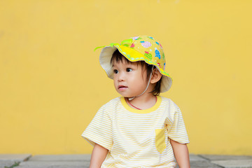 Portrait of happy Asian baby child girl. She wearing a yellow shirt and hat. Sweet smiling. On yellow background. Travel in the summer season concept. Baby aged 1 year and 4 months olds.