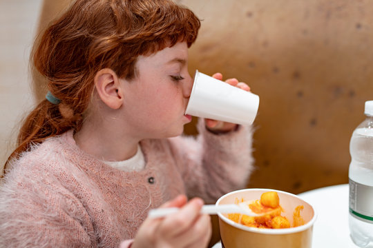 Bambina capelli rossi, che mangia e beve di gusto in una ristorazione, bar, fast food