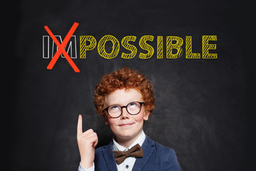 Child boy in glasses and school uniform looking at text possible on chalkboard background