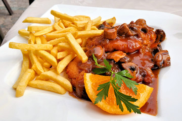 Traditional German Jagerschnitzel with a brown mushroom gravy and french fries. Close up view on a white plate.
