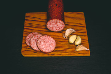 Top view of raw salami sausage food with slices and garlic in dark – Rustic food shot from above on a wooden board and a clean black background