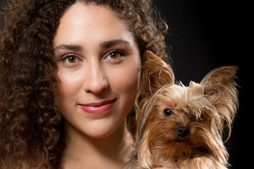 Closeup shot of a young latin lady holding her Yorkshire Terrier dog for a portrait. She is smiling to the camera.