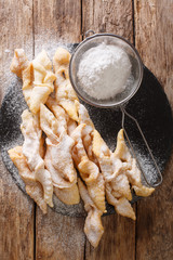 Freshly made Angel Wings Cookies with powdered sugar close-up. Vertical top view - obrazy, fototapety, plakaty