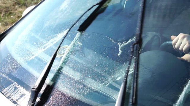 Glass washer nozzles splash on the windshield, wipers clean dirt and dust from the surface, close-up inside the cabin
