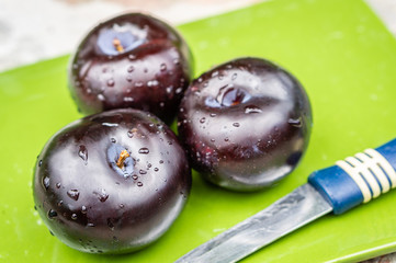 Three dark purple plum fruits and one cut  on a green plate