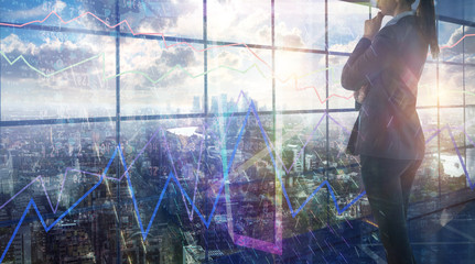 Young woman in suit in front of the glass screen which reflects business growth charts and diagrams and falling digits. Business background and City of London skyscrapers at the back