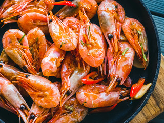Fried prawns with hot peppers in a frying pan on a wooden board. Table setting
