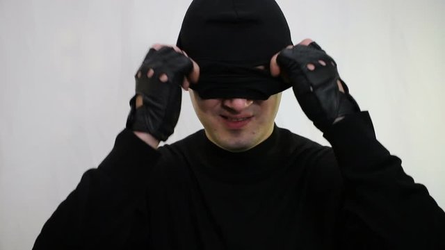 young cheeky caucasian man bandit with a smirk puts on a balaclava at the end of the video goes down, close-up