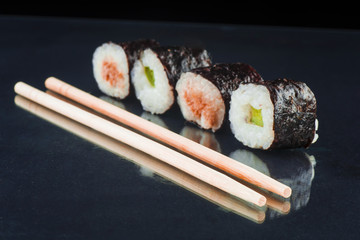 Sushi and chopsticks on a glass black background