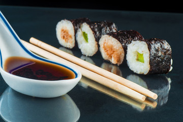 Sushi, chopsticks and sauce on a glass black background