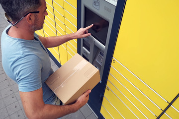 Man client using automated self service post terminal machine or locker to deposit the parcel for...