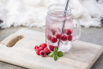 Home fizzy drink with ice and raspberry on a light background, selective focus. Photo of home made refreshing beverage