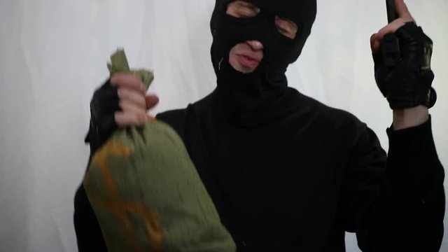 Young saucy caucasian robber with a gun dances with a bag of money and rejoices at the prey, close-up