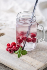 Home fizzy drink with ice and raspberry on a light background, selective focus. Photo of home made refreshing beverage