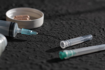 scattered pills jars of pills and syringes on a black background