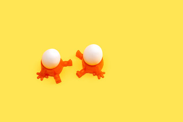 Two eggs in orange egg cup, isolated on yellow background  with copy space
