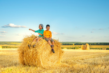 Children have fun  sit  on a haystack on a sunny day in the field.