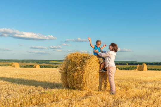A grandmother with a grandson puts on a haystack on a field on a sunny day.  Grandson delighted, they have fun together.