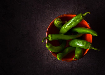 A few green hot peppers shot from above on a dark stone background. Plenty of space for text.