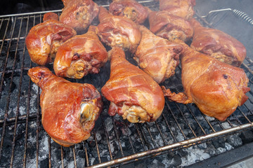 BBQ of large golden brown turkey drum sticks on an outdoor coal grill