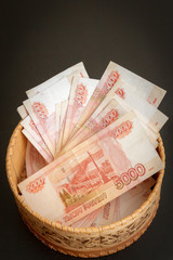 A lot of banknotes worth five thousand rubles are in a round wooden wicker box.