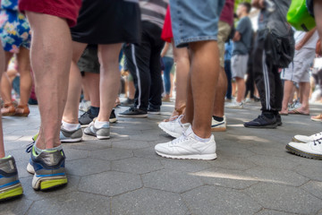 Crowd of standing people watching and event, shorts, feet and legs on a casual weekend summer day