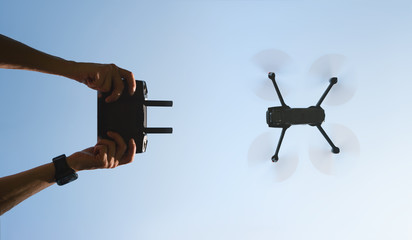 Remote control in men hands and the silhouette of a flying drone. View from the bottom