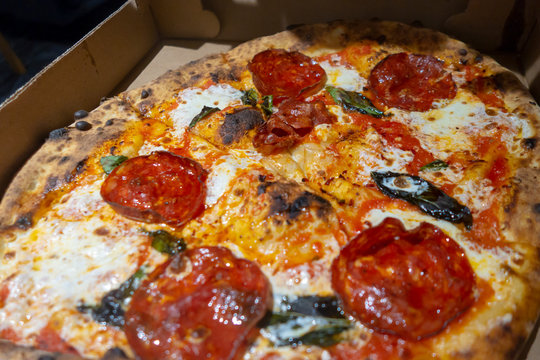 Single serving brick oven Neapolitan-style pizza with spicy Hot Soppressata, fresh mozzarella, fresh basil in a bizza box