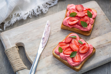Toast with strawberry on wipped cream on a wood board on light background. Summer traditional homemade dessert.