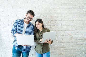 Colleagues Working With Laptops Against Wall In Office