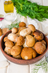 Fresh forest white mushrooms in a bowl with spices and fresh herbs on a wooden background