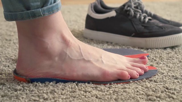 Female feet standing on the orthotics near sneakers slow mo